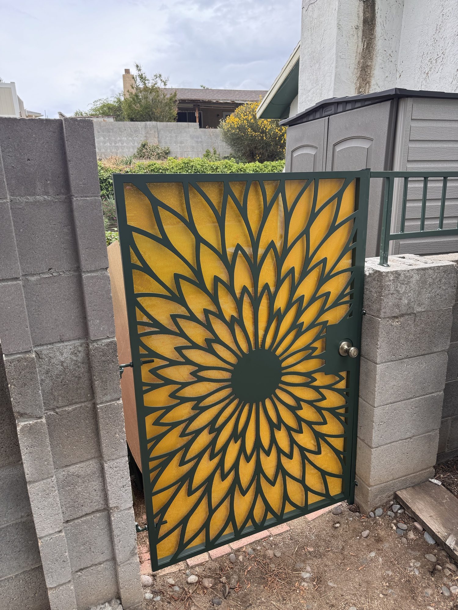Custom plasma-cut steel garden gate with a stylised sunflower bloom over a gold perforated mesh backing, fabricated by Sandbar Fabrication