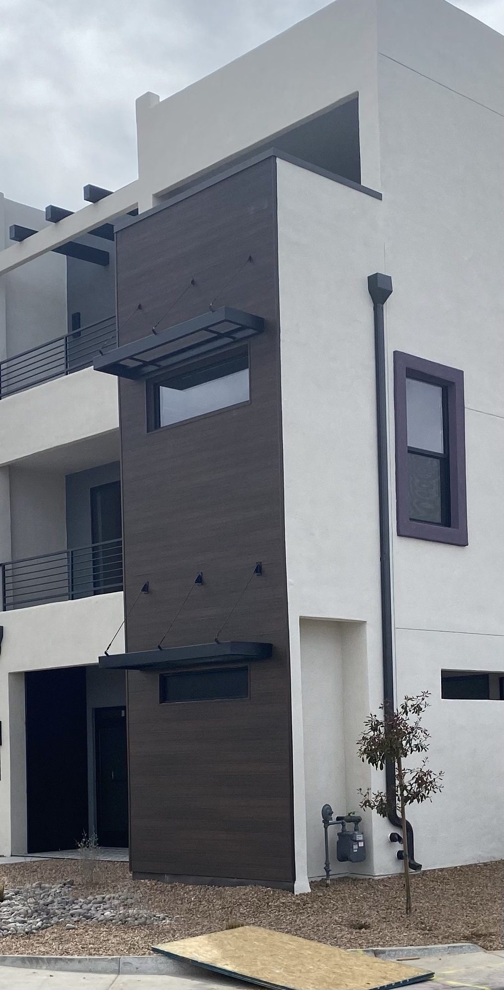 Cantilevered steel window awnings with tension rod supports and matching balcony railings on a modern home